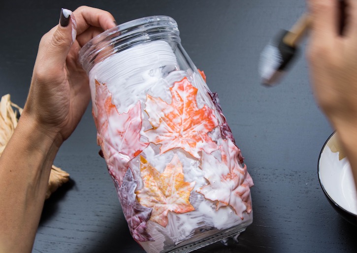 Mason jar covered in fall colored leaves and mod podge glue. 