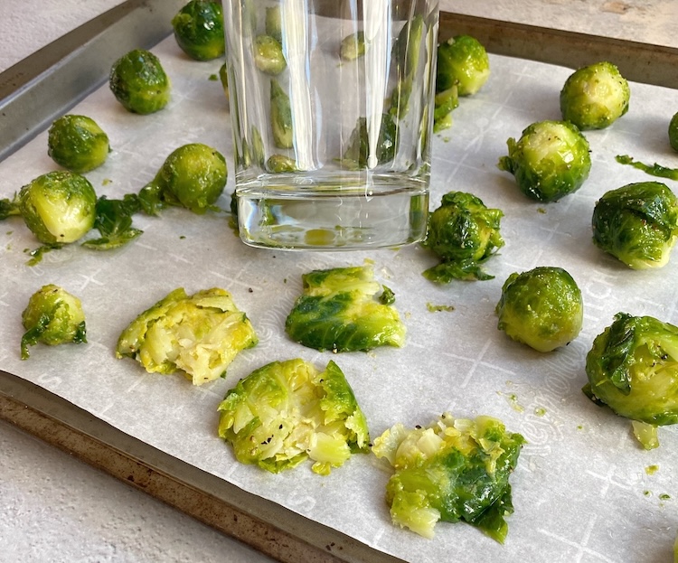 Brussels sprouts being smashed with the bottom of a glass cup to make them crispy once roasted in the oven.