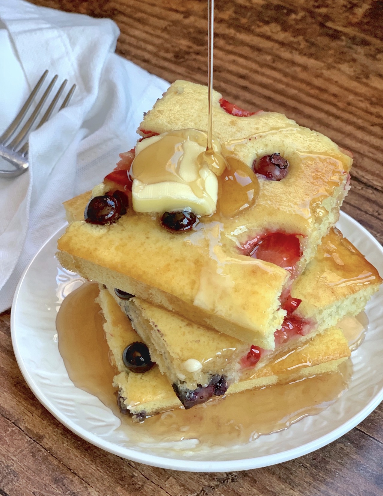 Sheet pan pancakes on a plate loaded with butter and syrup to make a yummy breakfast to feed a crowd in the morning. 