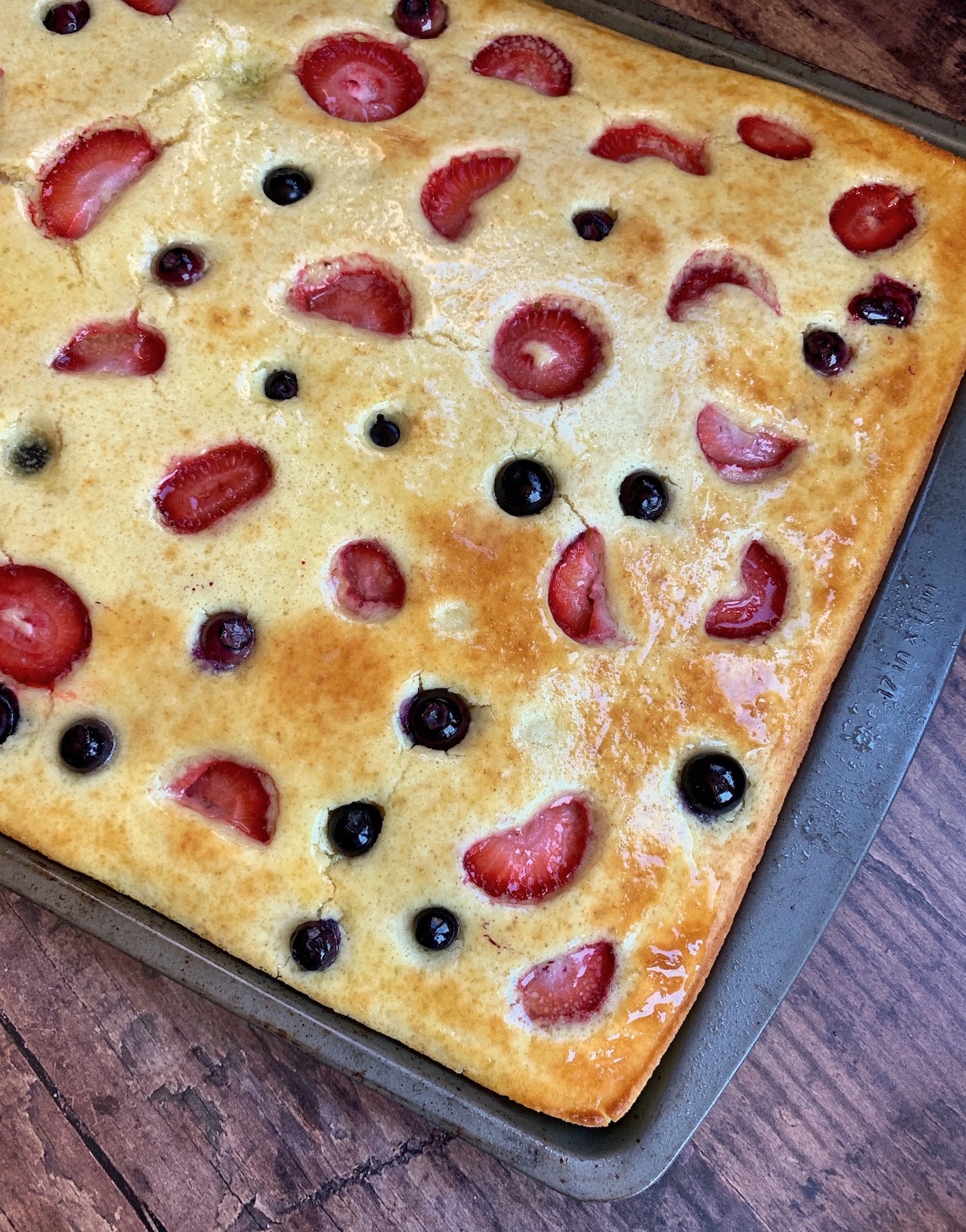 Golden brown pancakes brushed with butter on a sheet pan after baking to make breakfast for a crowd. 