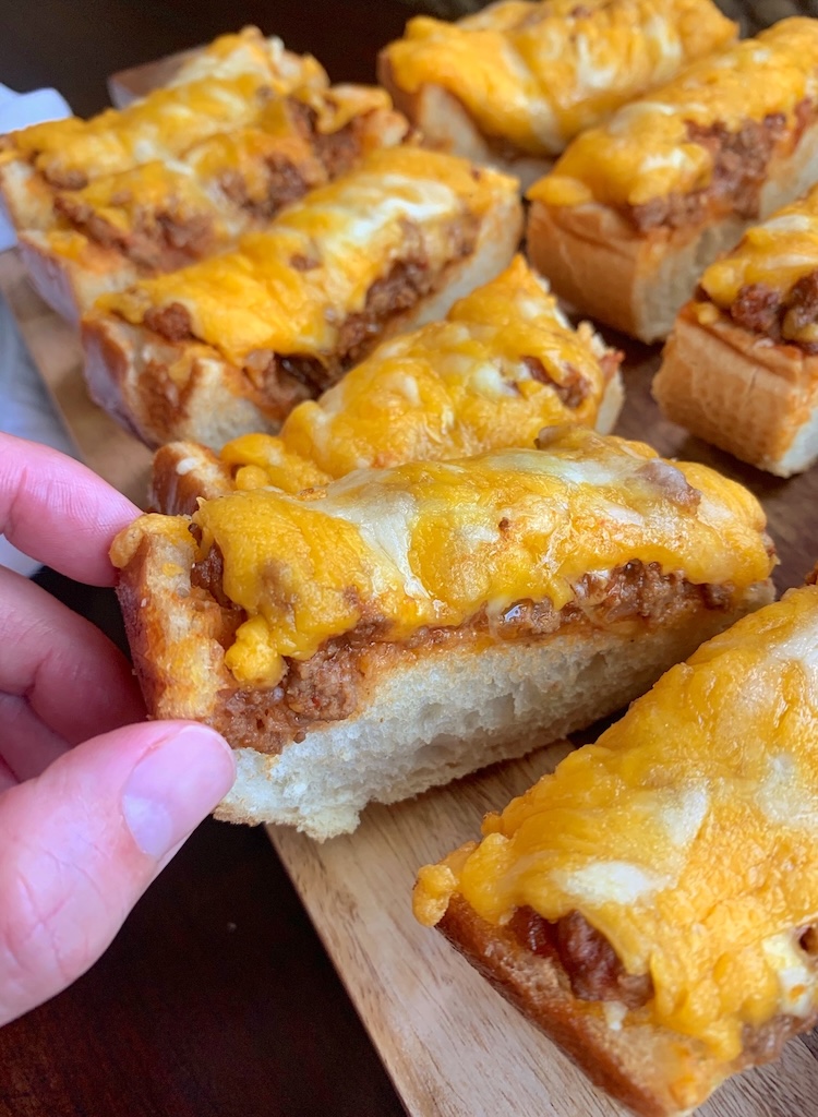 Close up view of Sloppy Joe French Bread pizza being grabbed from a serving dish. 