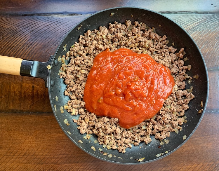 Cooked and browned ground beef in a pan topped with a can of Manwich Sloppy Joe Mix. 