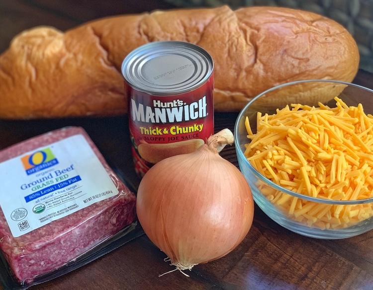 Ingredients for making Sloppy Joe Pizza including a loaf of French bread, 1 pound ground beef, a can of Manwich, a cup of shredded cheddar cheese, and an onion. 