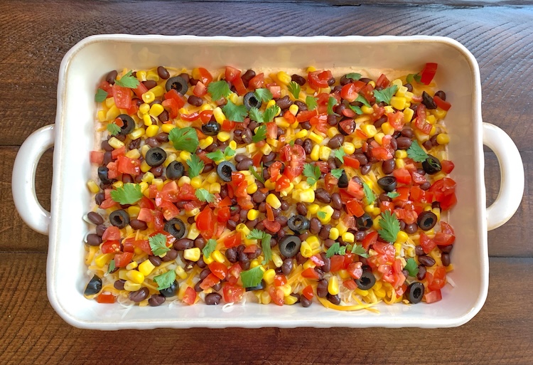 Cold Cream Cheese Taco Dip topped with beans, corn, diced tomatoes, olives, and cilantro making for a crowd pleasing party appetizer for parties and more. 
