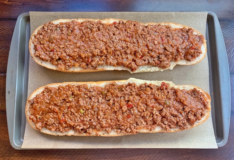 French bread sliced in half on a baking sheet topped with a Sloppy Joe Ground Beef Mixture. 