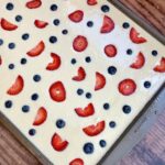 Pancake batter on a sheet pan topped with fresh sliced strawberries and blueberries ready for the oven to make breakfast for a crowd.