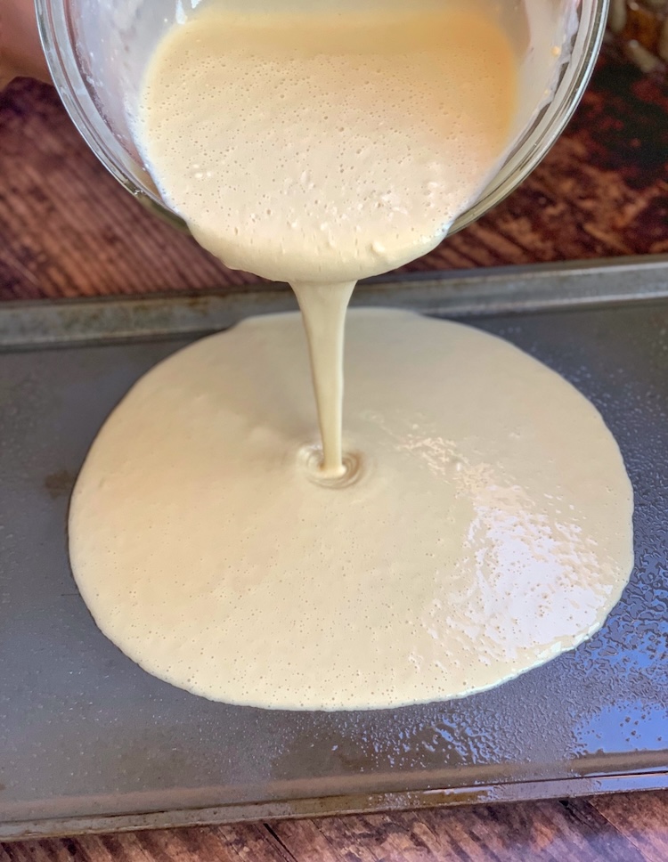 Bisquick pancake batter being poured onto a greased sheet pan to make oven baked pancakes. 