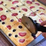 Baked pancakes on a sheet pan being cut with a pizza cutter to make individual slices to feed a crowd at breakfast time.